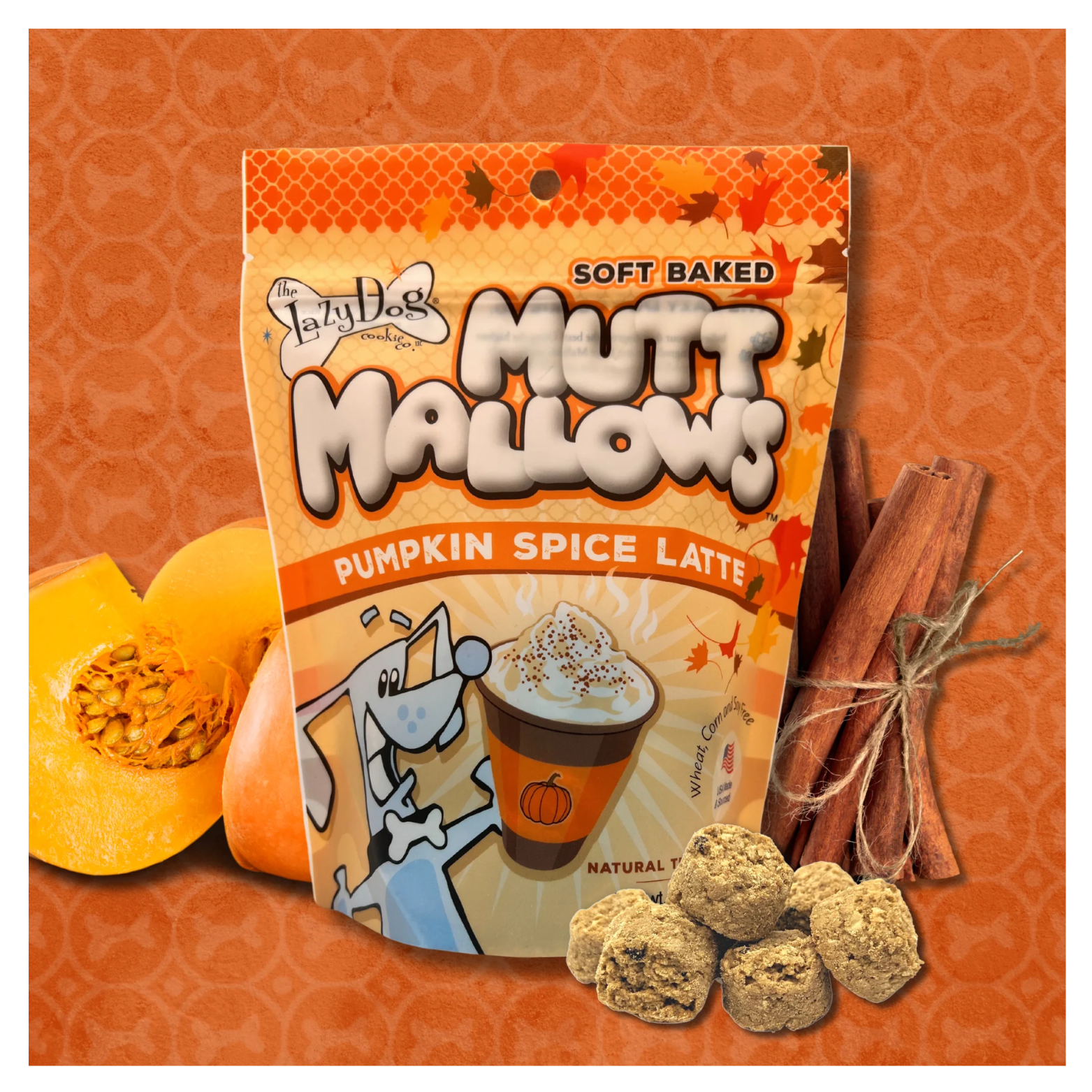 Bag of The Lazy Dog Cookie Company “Soft Baked Mutt Mallows” Pumpkin Spice Latte dog treats displayed on an orange background with fall leaves, surrounded by a halved pumpkin, cinnamon sticks, and several round beige dog treats in the foreground.