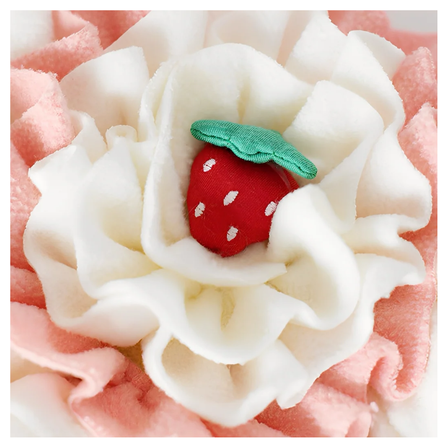 Close-up of the cupcake’s cream fleece center showing a soft red plush strawberry with a green leaf nestled among ruffled fabric layers designed for hiding treats.