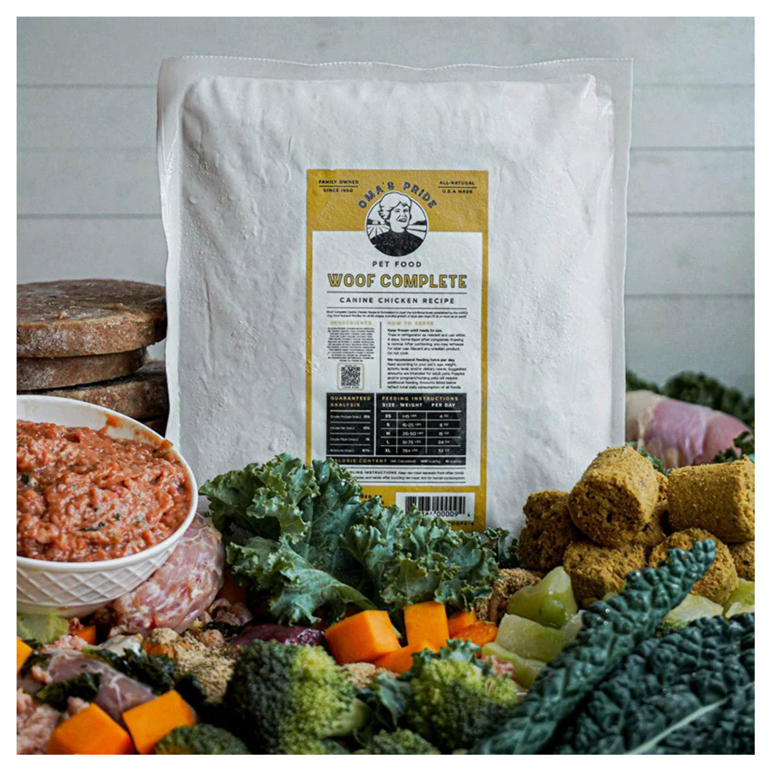 A large package of Oma’s Pride Woof Complete Chicken Recipe surrounded by raw ingredients including vegetables, chicken, and frozen portions on a countertop.