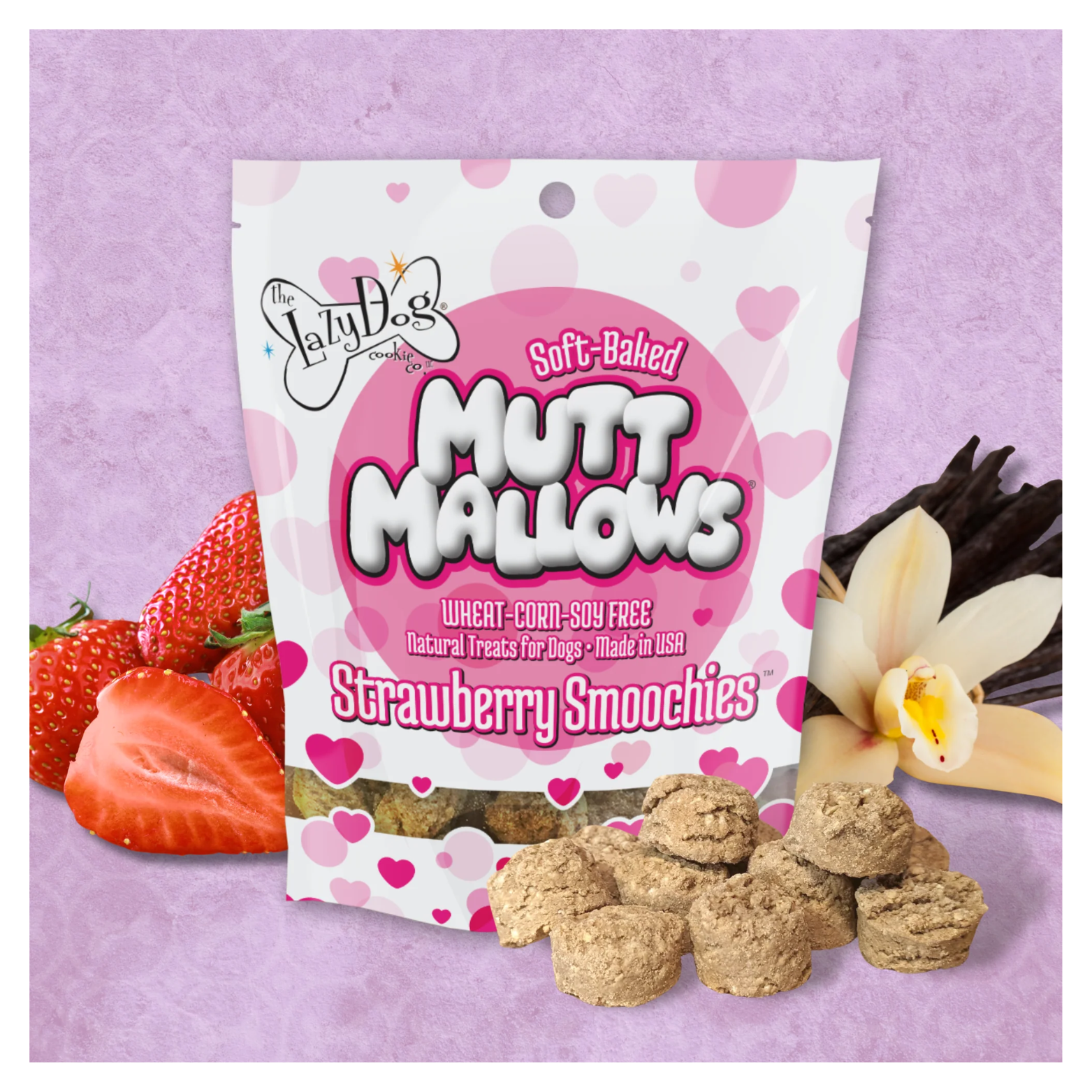 A bag of Strawberry Smoochies Mutt Mallows standing on a pink background, surrounded by fresh strawberries, vanilla beans and flower, with several soft-baked treats displayed in front.