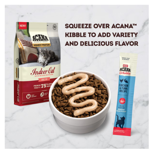 Bowl of dry cat kibble topped with a zigzag drizzle of creamy chicken-and-tuna lickable treat, shown beside an ACANA Indoor Cat kibble bag and an ACANA Lickables Chicken & Tuna Recipe sachet on a marble surface.