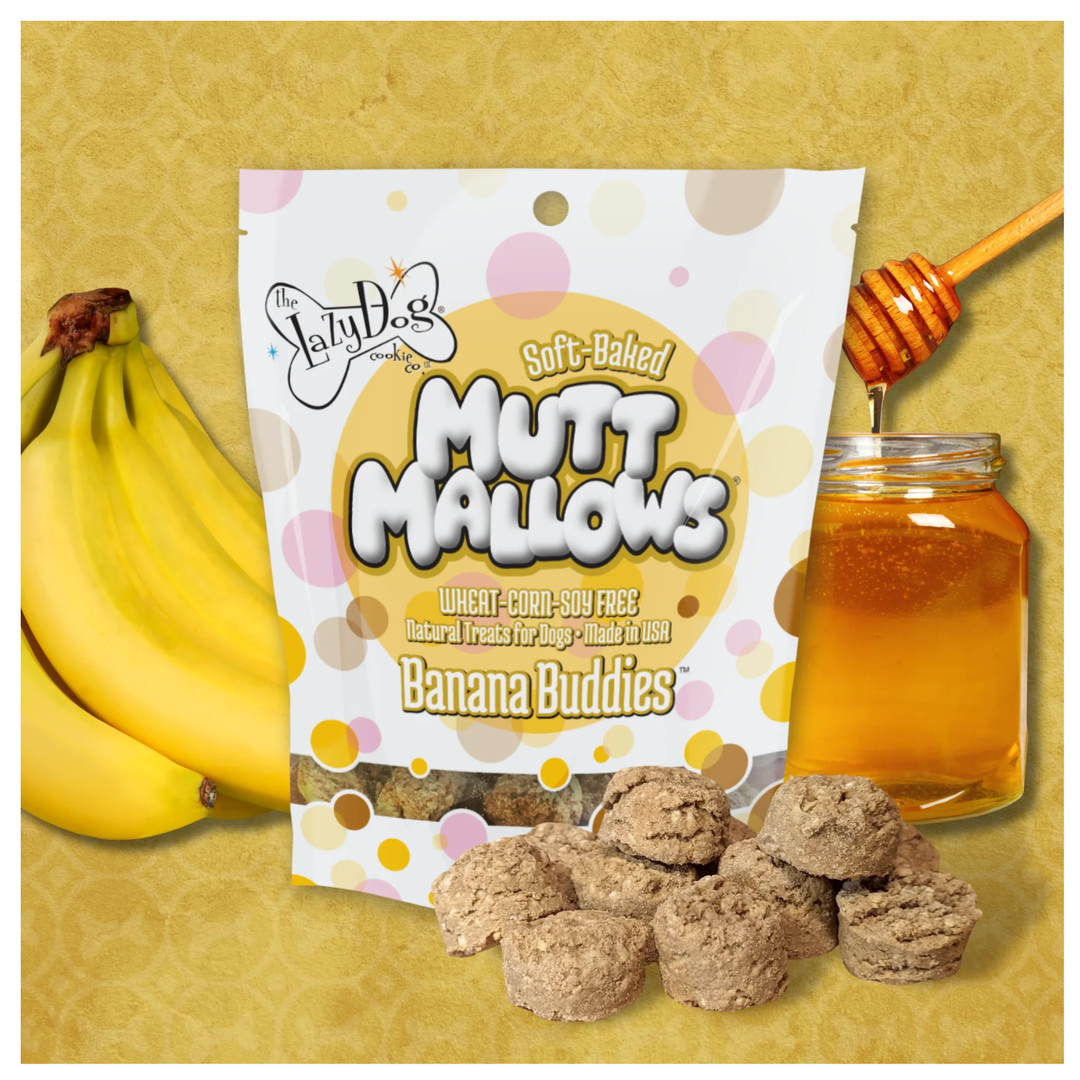 Banana Buddies Mutt Mallows bag displayed upright on a yellow background, flanked by a bunch of bananas on the left and a jar of honey with a honey dipper on the right, with several round dog treats arranged in front.