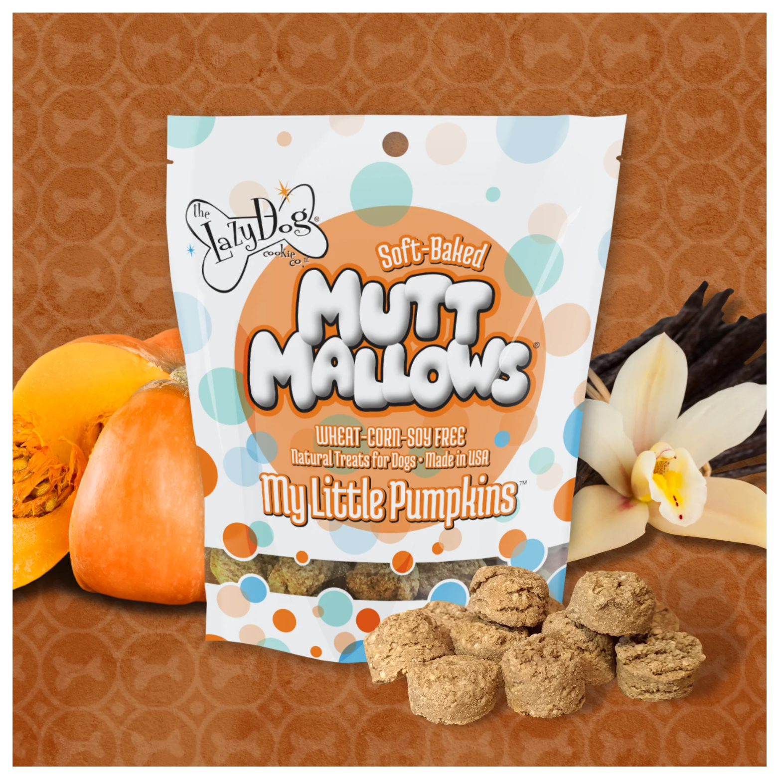 Bag of “My Little Pumpkins” Mutt Mallows displayed on an orange patterned background with pumpkins, vanilla flowers, and several round soft baked dog treats arranged in front of the package.
