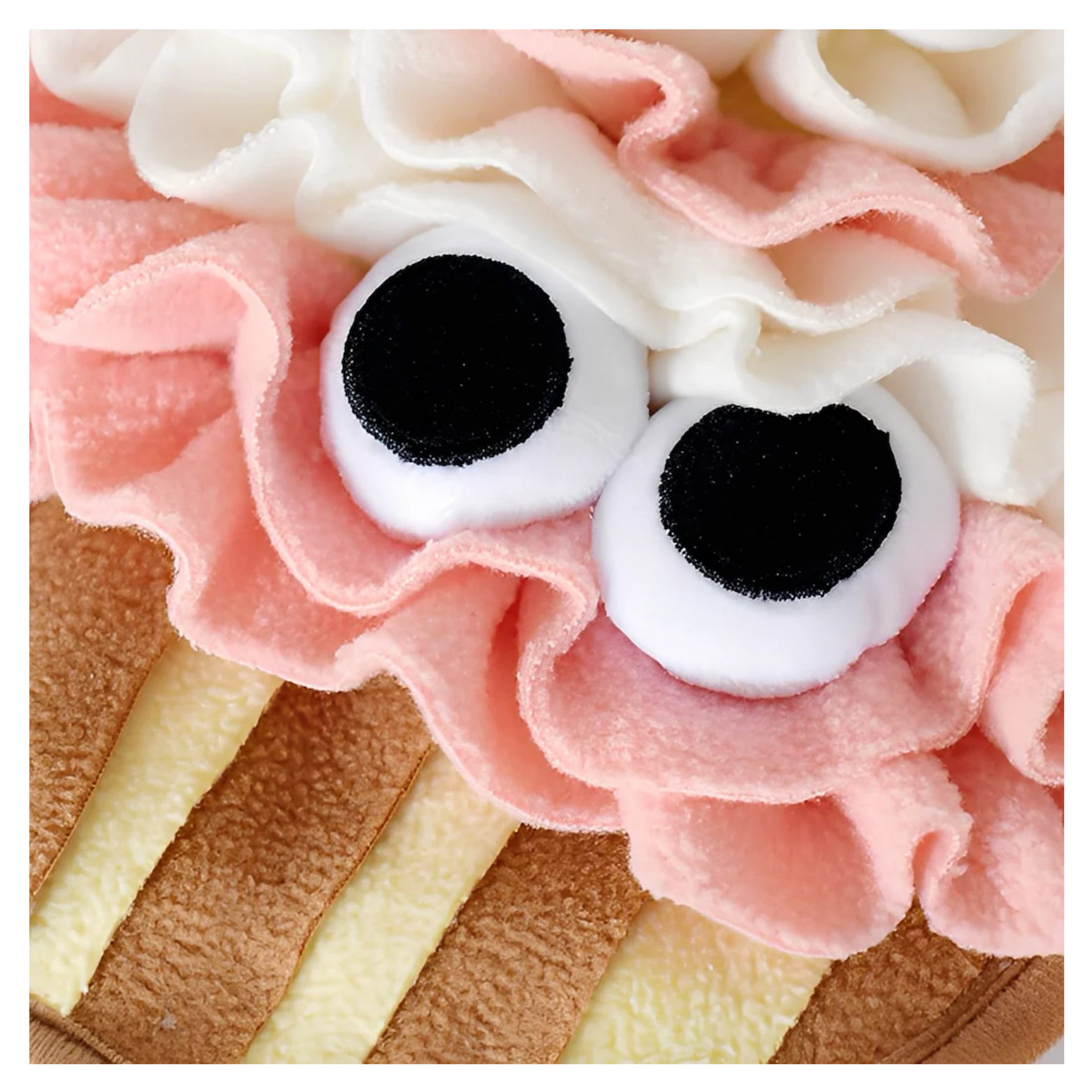 Close-up of the front of the cupcake snuffle mat highlighting the large black-and-white plush eyes and the textured tan cupcake wrapper below.