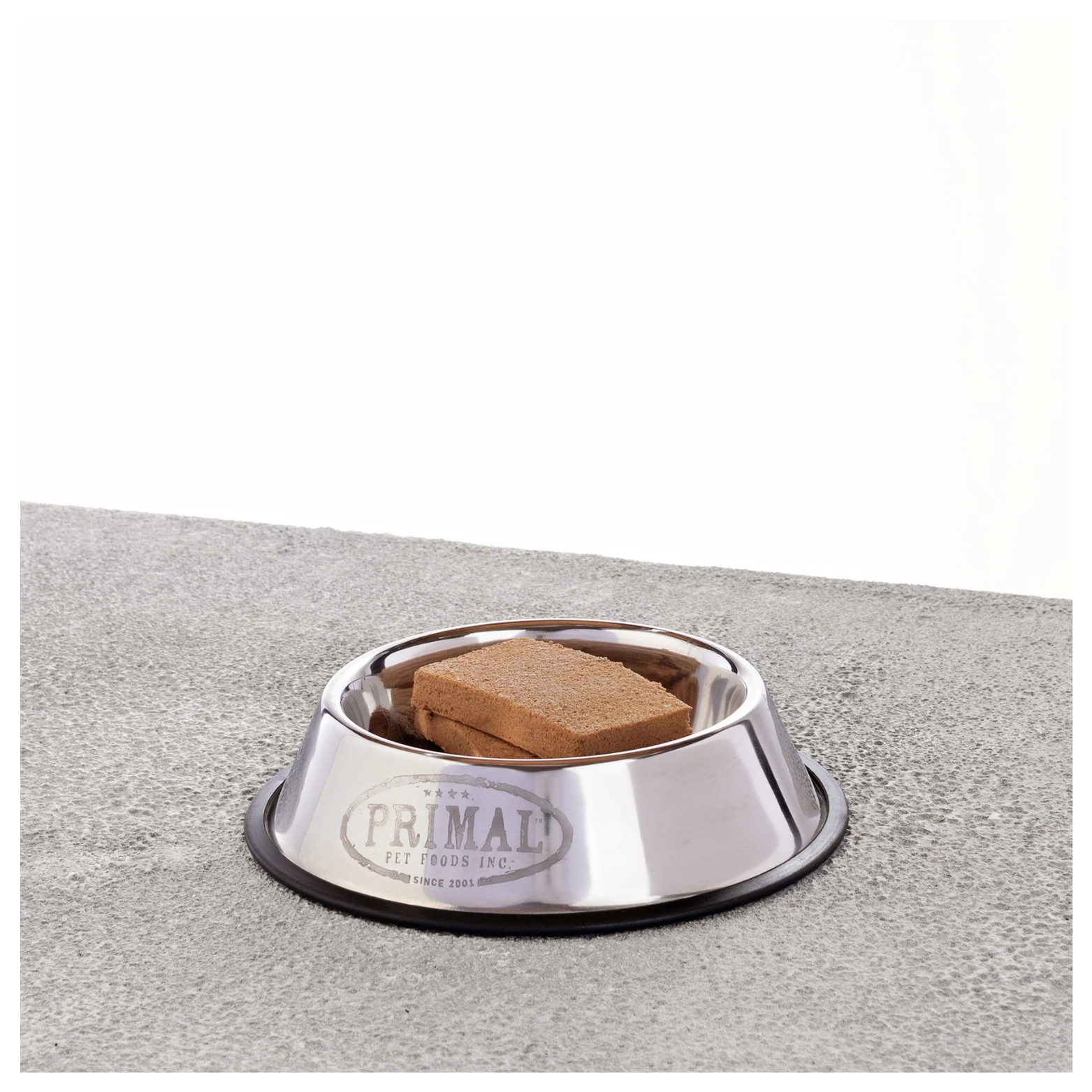Stainless steel dog bowl containing two rectangular frozen raw patties on a textured gray surface.