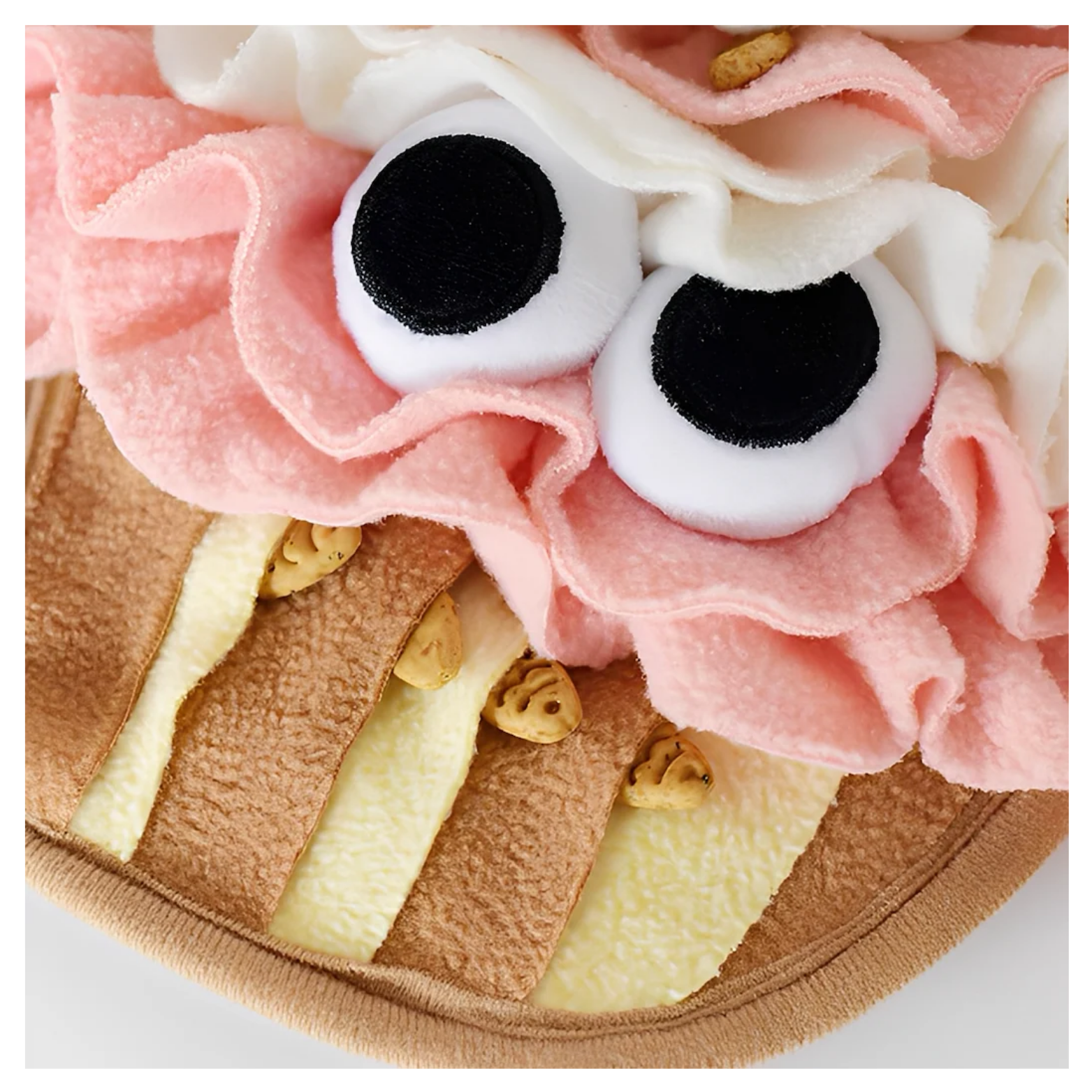 Detailed close-up of the lower cupcake base with alternating tan and yellow fleece strips, with small treats tucked between the layers for foraging play.