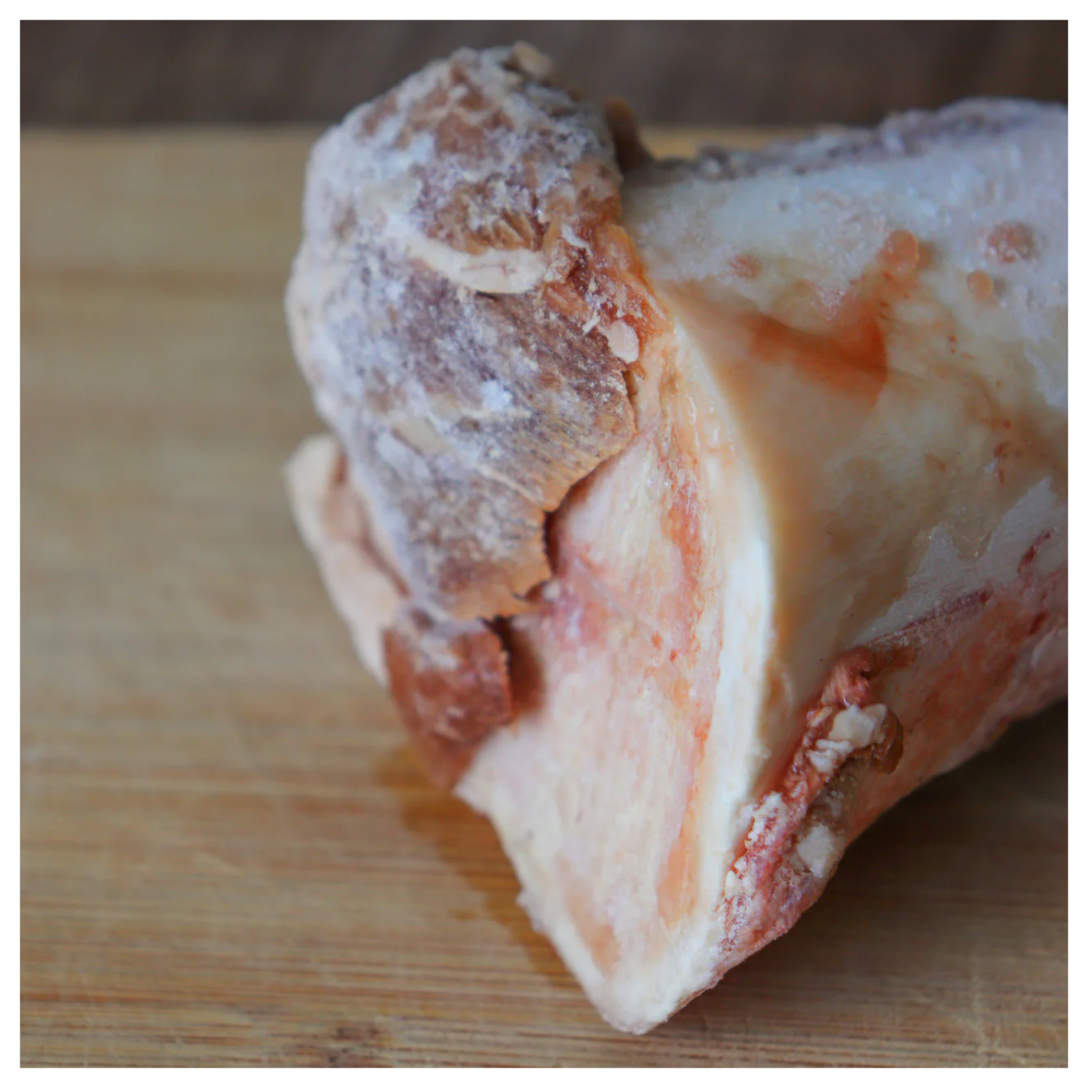 Close-up of a frozen beef marrow bone resting on a wooden surface with frost visible on the exterior.