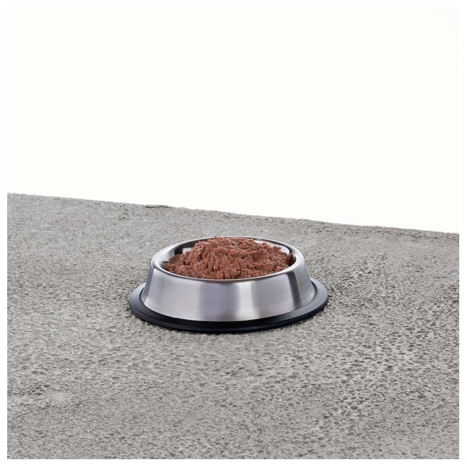 Stainless steel pet bowl filled with thawed raw cat food with a soft ground texture on a gray surface.