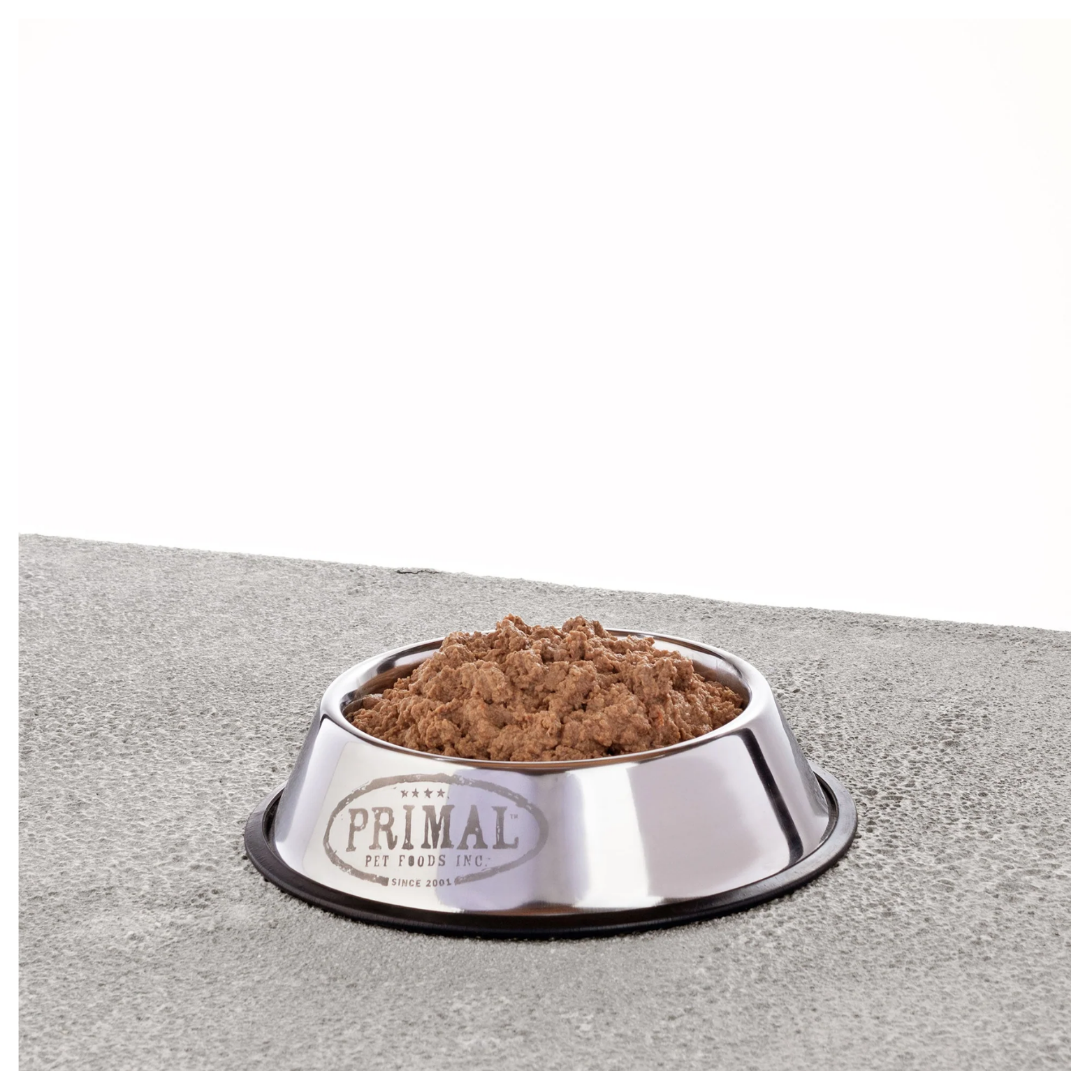 Stainless steel dog bowl filled with thawed raw dog food with a soft ground texture on a gray surface.