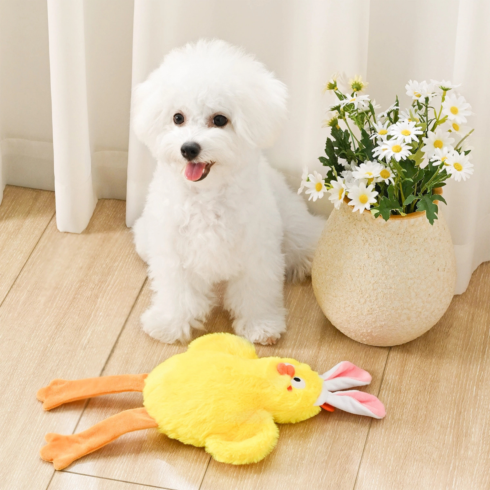 White dog with a yellow plush toy on a wooden floor next to a vase with flowers.